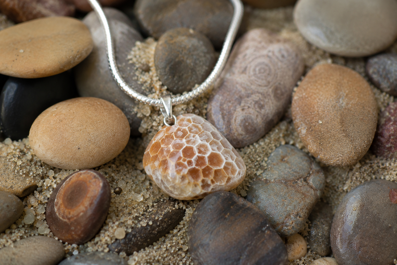 Petoskey stone pendant necklace with sterling silver setting displayed on polished beach stones